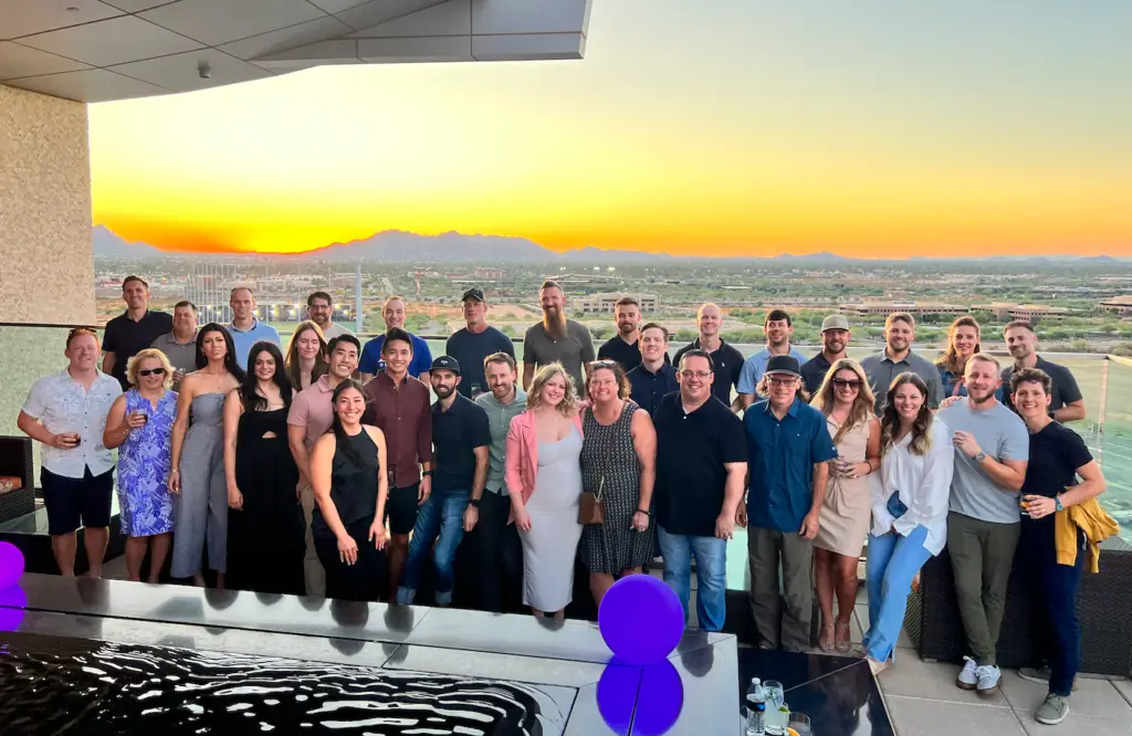 Open Door Capital team standing on a rooftop at sunset, smiling together with a vibrant sunset in the background.